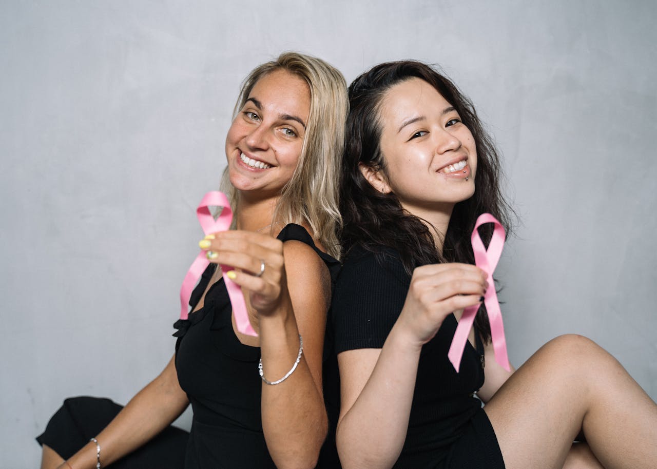 Two women holding pink ribbons to promote breast cancer awareness and support.