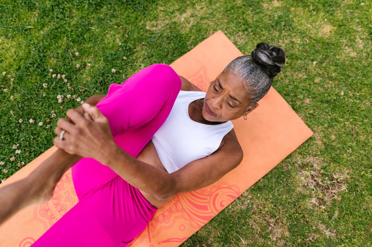 about-01 Elderly woman performing yoga stretch on grass for wellness.